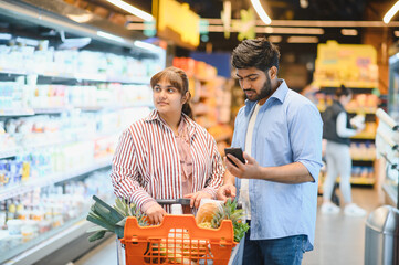 Indian couple using smartphone while shopping in grocery store