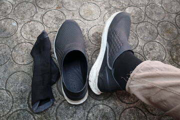 A person's feet, with one shoe and sock on and the other shoe and sock off, resting on a patterned concrete floor, representing the concept of comfort and casual wear.