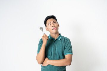 Portrait of a thoughtful young man holding a spoon and looking upwards with a reflective expression...