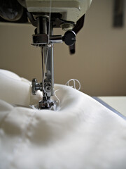 Macro shot of an industrial sewing machine stitching white fabric, detail of textile manufacturing and garment production.