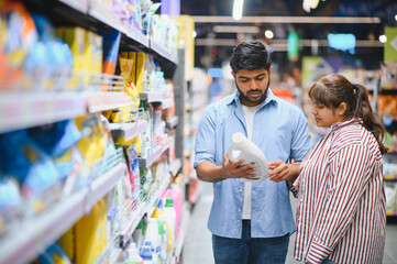 Indian couple choosing cleaning product in supermarket household chemicals aisle