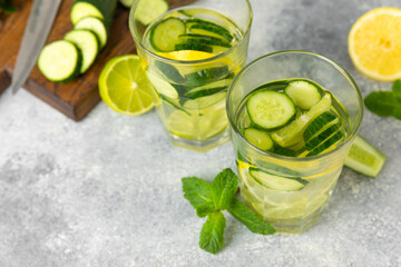 Cucumber water with lemon, lime and mint on a wooden table. Water infused with sliced ​​cucumber in a drinking glass. Tonic refreshing drink. Cucumber lemonade.Summer natural cooling drink.Copy space