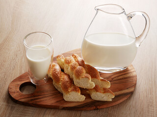 A breakfast setting with bread, milk in a glass and a pitcher, all arranged on a wooden board. The...