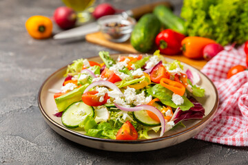 Cucumber salad on a wooden background.Homemade salad with fresh vegetables, cucumber, tomato, sweet pepper and lettuce in a plate.Vegetarian spring salad.Vegetarian diet.Healthy eating.Space for text