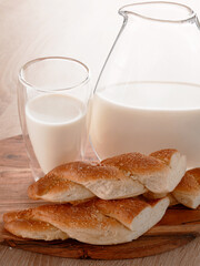 A breakfast setting with bread, milk in a glass and a pitcher, all arranged on a wooden board. The scene is well-lit and suggests a simple, healthy meal.