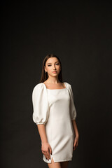Woman on a dark background in a studio, she is wearing a long white dress