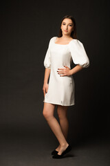 Woman on a dark background in a studio, she is wearing a long white dress