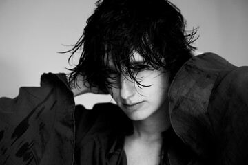 Monochrome artistic portrait of person in dark clothing with hand near face and dramatic lighting