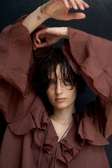 Young woman in burgundy hoodie with hands raised above head creating dramatic shadow portrait