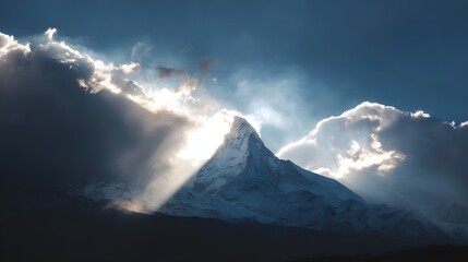 Sunbeams pierce through clouds illuminating a snow-capped mountain peak.