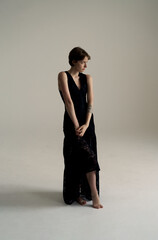 Elegant brunette model in formal black gown standing gracefully in minimalist studio with dramatic...