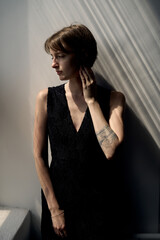 Fototapeta premium Contemporary portrait of woman in black sleeveless dress with dramatic window light creating artistic shadows