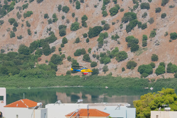 Blue and yellow firefighting helicopter flying over lake to collect water for extinguishing fire
