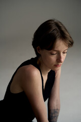 Fototapeta premium Young woman in black sleeveless top looking down thoughtfully in warm studio lighting