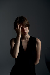 Young brunette woman in black dress touching forehead with fingers in thoughtful pose against...