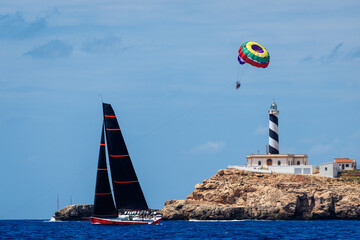 Nautical scene of a sailboat sailing near the lighthouse of Cala Fiquera, Mallorca and a parachute...