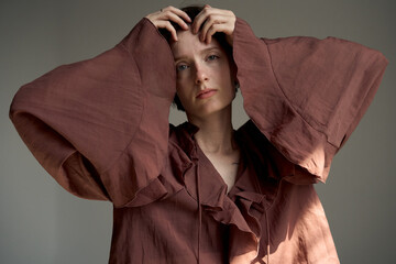 Contemporary portrait of woman in rust-colored oversized shirt with hands raised in expressive pose...