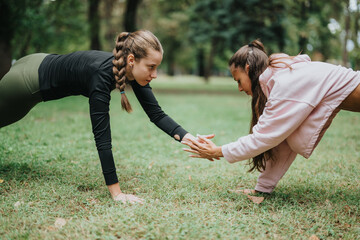 Female fitness enthusiasts engaged in an interactive push-up exercise in a park. Health and...