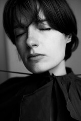 Dramatic black and white portrait of young woman with short dark hair wearing elegant black bow...
