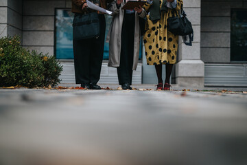 A group of people in business attire gathering outside to review documents, strategize, and discuss...