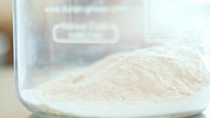 A macro close-up shot shows a white chemical powder being added to a glass beaker in a clean, modern laboratory for a scientific or pharmaceutical experiment. - Powered by Adobe