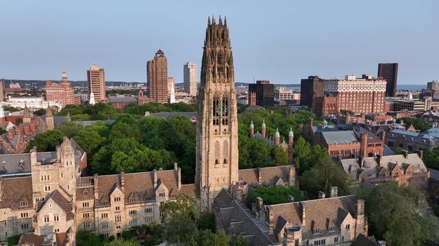 Aerial approaching shot of Harkness Tower at Yale old campus university of New Haven. American City in Connecticut at sunset. Summer day with green trees. Connecticut Financial Center In background.