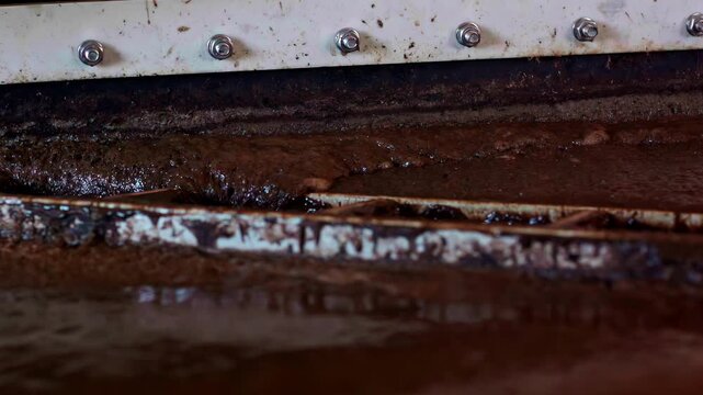 A close-up shot shows an industrial machine separating dirt and solids from a thick sludge during a wastewater cleaning and purification process at a treatment plant.