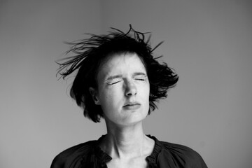 Young woman with tousled hair experiencing intense emotion against neutral background in studio...
