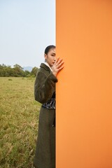 Woman peeking from behind an orange wall in a green field.