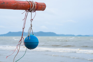 Blue buoy hanging from a red pole on a beach with an ocean background and distant hills on a cloudy...