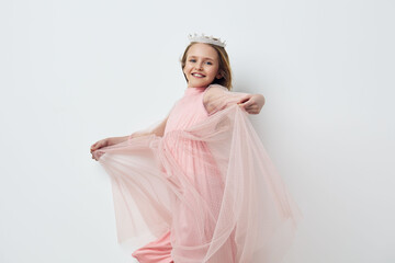 Joyful young girl in a pink dress with flowy fabric, smiling and posing against a minimalist white...