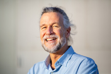 Joyful senior man smiling in sunlight with blue shirt