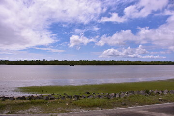 The wide Bakkhali River estuary in Cox's Bazar, viewed from the protective embankment on a dramatic, cloudy day during the monsoon season.