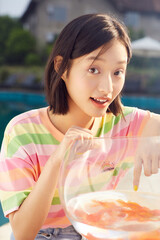 Young woman interacting with a fishbowl outdoors.