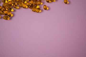 Close-up of scattered golden capsules on a soft pink background, showcasing the texture and color...
