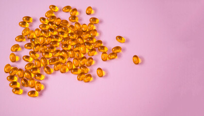 Bright orange gel capsules scattered on a soft pink background, showcasing the vibrant color and...