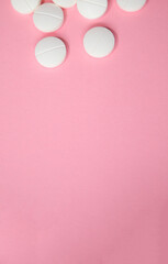 White round pills scattered on a soft pink background, creating a visually appealing composition,...