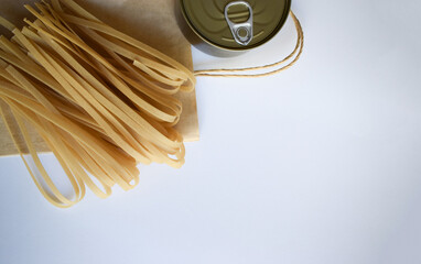 Raw pasta strands arranged beside a can on a brown paper surface, with a clean white background,...