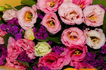 Bright and delicate bouquet of fresh flowers — pink and white lisianthus combined with purple statice, wrapped in yellow craft paper. Close-up, horizontal composition, isolated on a light background. 