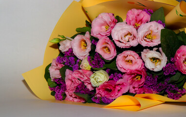 Bright and delicate bouquet of fresh flowers — pink and white lisianthus combined with purple statice, wrapped in yellow craft paper. Close-up, horizontal composition, isolated on a light background. 