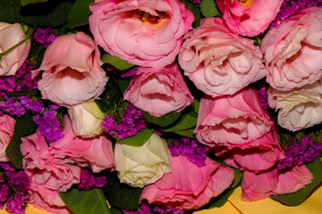 Bright and delicate bouquet of fresh flowers — pink and white lisianthus combined with purple statice, wrapped in yellow craft paper. Close-up, horizontal composition, isolated on a light background. 