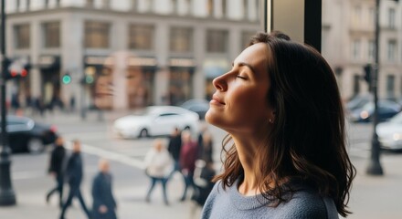 Obraz premium A serene woman with closed eyes enjoys a moment of peace by a window overlooking a bustling city street.