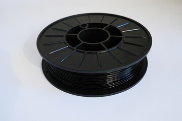 Black filament spool for 3D printing, suitable for various projects at a workspace