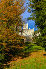 Trakošćan Castle is beautifully framed by vibrant autumn trees, with golden foliage on one side and deep green on the other. 