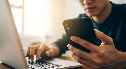 Man Using a Smartphone and Laptop in the Office Working on a Project Focusing on Digital Technology and Online Communication