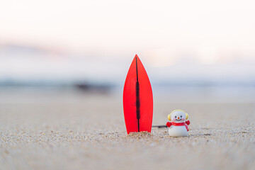 Sandy Christmas Snowman is watching the waves, standing on beautiful beach with a surf board -...