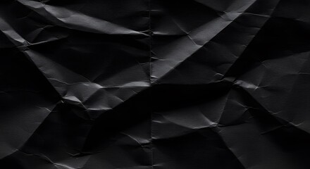 Fototapeta premium Wrinkled black paper displays sharp creases varied shadows highlighting the textural complexity and light play