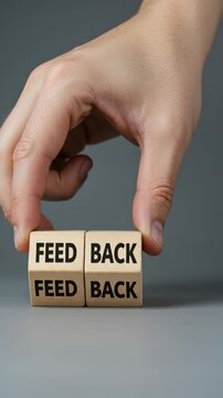 Feedback concept: Hand holding wooden blocks with "FEED BACK" message over gray backdrop, demonstrating importance of receiving criticism