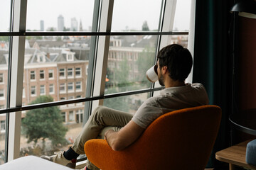 man drinking coffee in a chair with attic window and view on Amsterdam