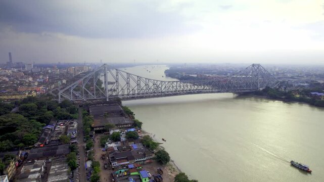 A drone aerial movement shot of the moving vehicles on the busy, iconic Howrah Bridge over the holy Ganges or Hooghly river in kolkata or Calcutta city, india on a cloudy, rainy day